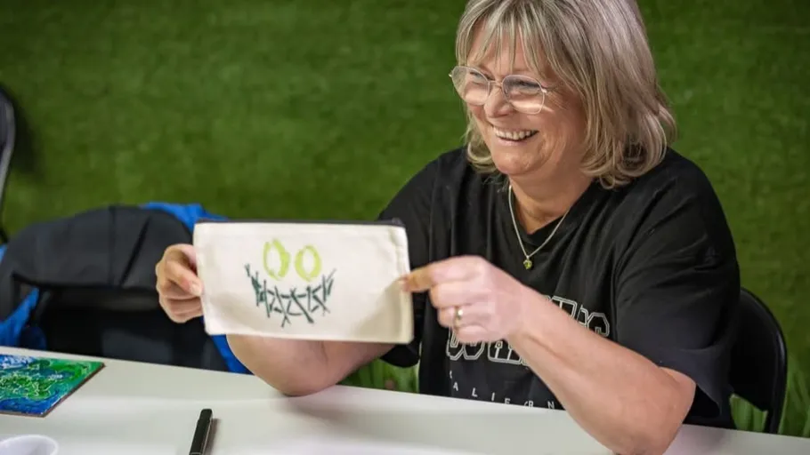 Frau hält bemalte Leinwand lächelnd drinnen.