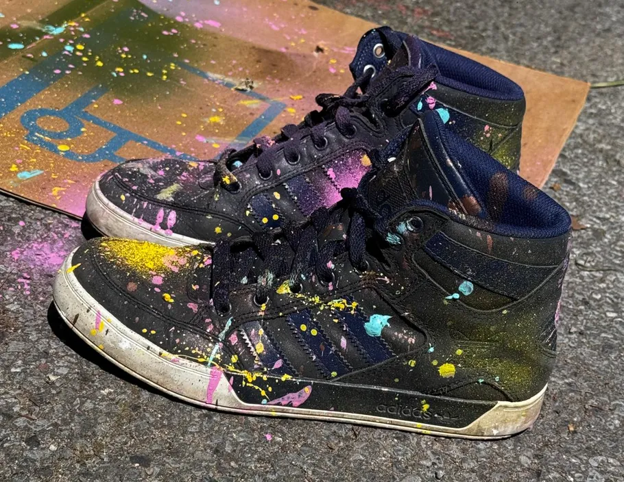 Mit Farbe bespritzte Turnschuhe auf Betonoberfläche.