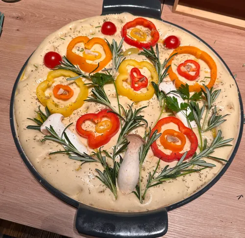 Unbaked focaccia with vegetables on a round tray.