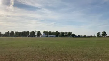 Weißes Zelt auf Grasfeld unter blauem Himmel.