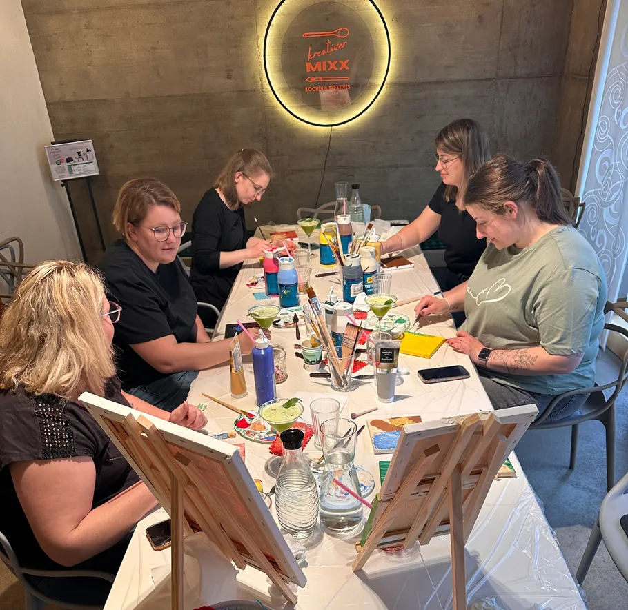 Frauen malen gemeinsam an einem Tisch drinnen.