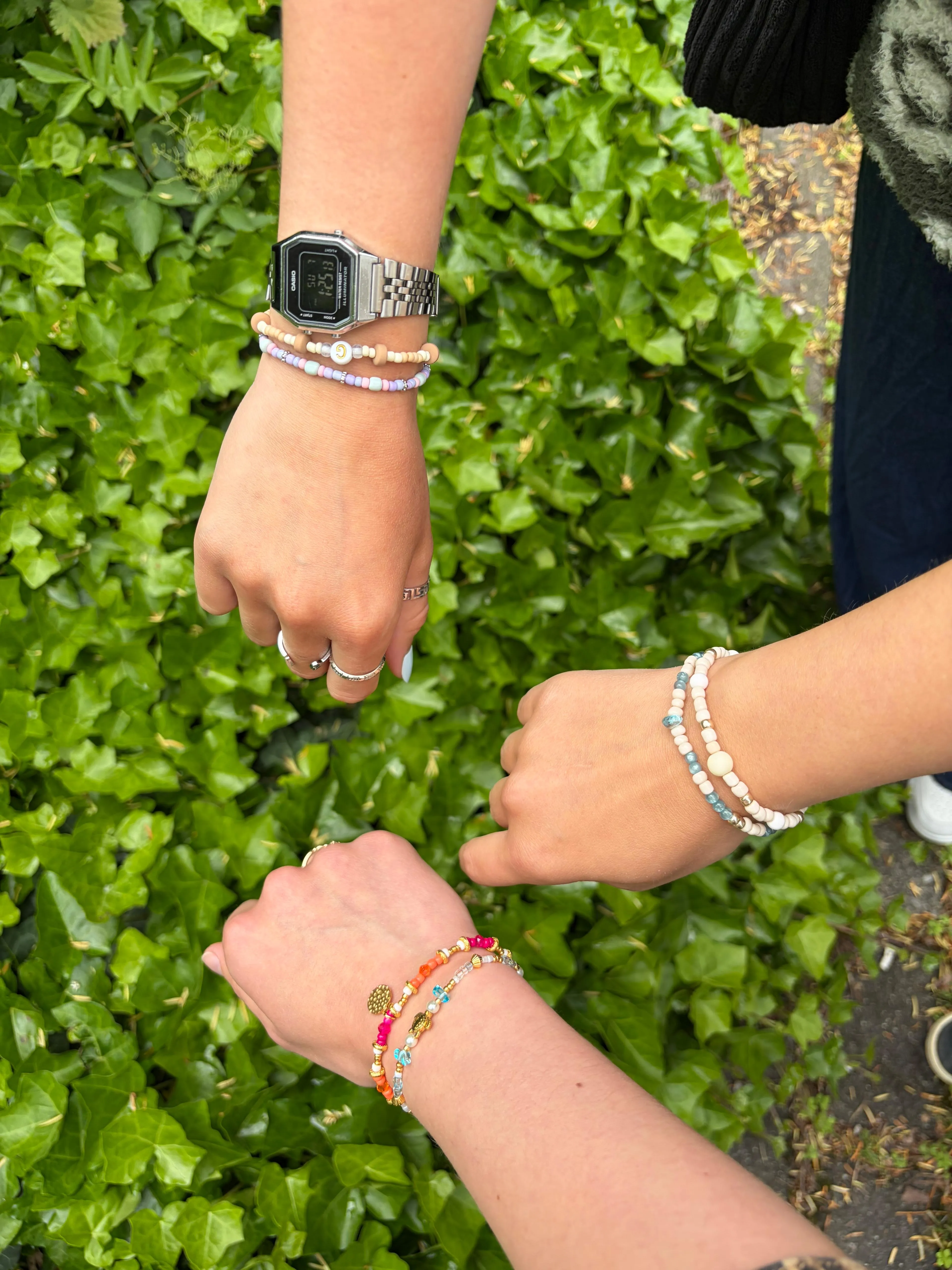 Drei Hände mit Armbändern über grünen Blättern.