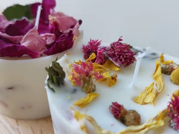 Zwei Kerzen mit getrockneten Blumen auf hellem Hintergrund.