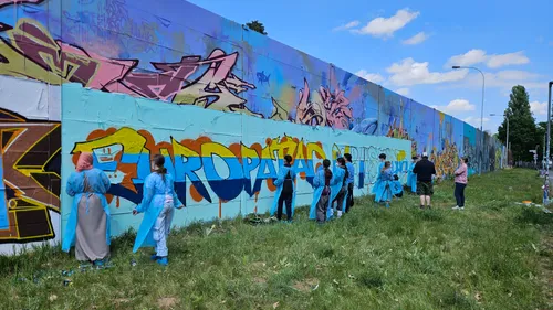 Menschen malen Graffiti auf einer langen Außenwand.