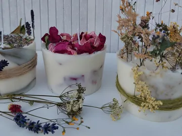 Drei dekorative Kerzen mit getrockneten Blumen neben Kräutern.