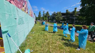 People painting graffiti on a wall outdoors.