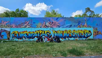 Colorful graffiti wall with people sitting grass.