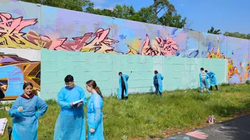 People paint graffiti wall with light blue paint.