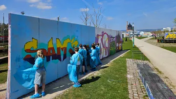Children painting graffiti on a wall outdoors.