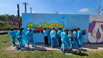 Children painting graffiti on wall outdoors.