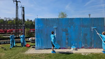Kinder bemalen draußen eine große blaue Wand.