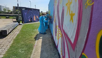 Personen malen bunte Wandbilder im Freien an eine Wand.