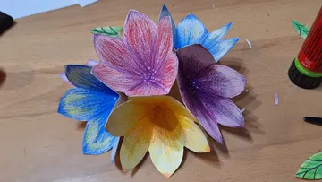 Bunte Papierblumen auf einem Holztisch.
