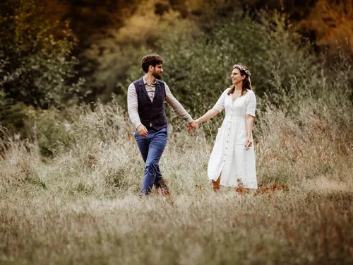 A couple holds hands and walks through high meadows.