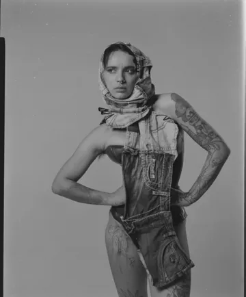 Person posiert in Denim mit Tattoos im Studio.