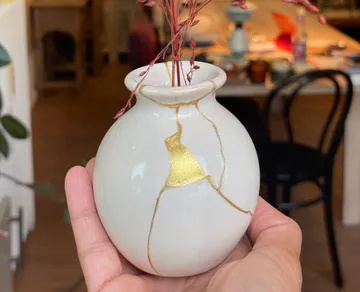 Hand hält weiße Vase mit goldenen Reparaturstellen.