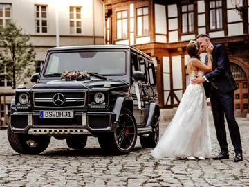 Hochzeitenparr, küssendes Paar vor einem schwarzen SUV.