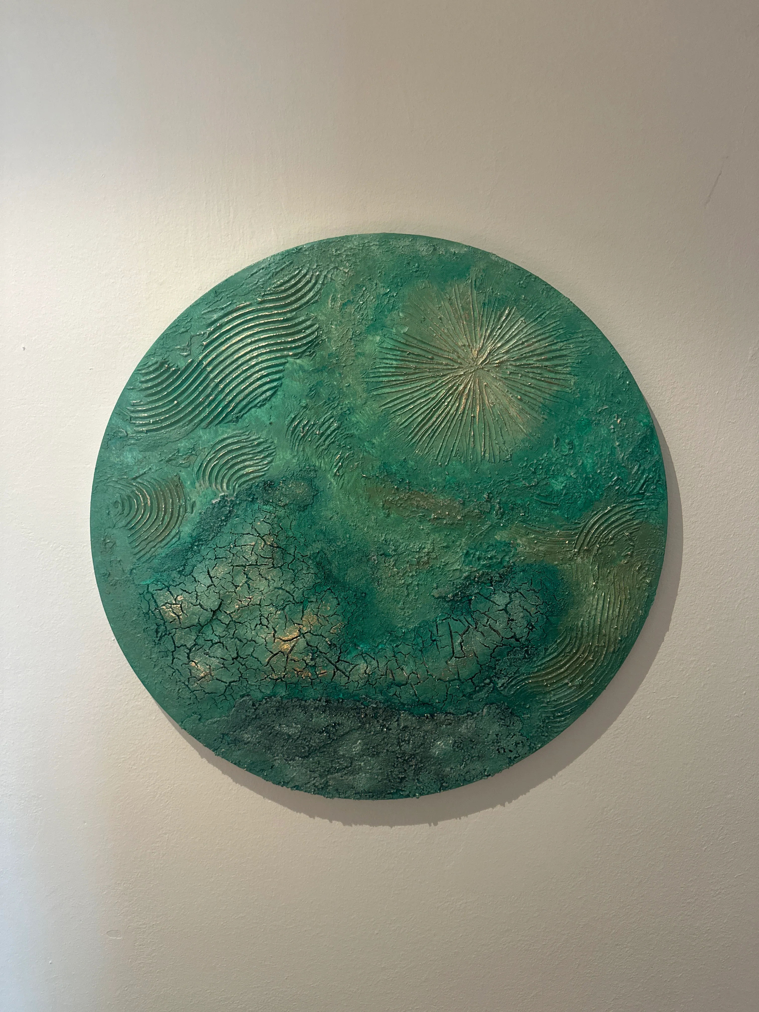 Rundes grünes strukturiertes Kunstwerk an Wand.