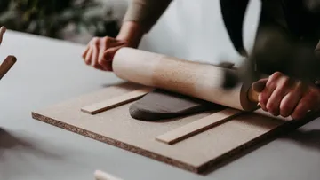 Hands rolling clay on wooden board.