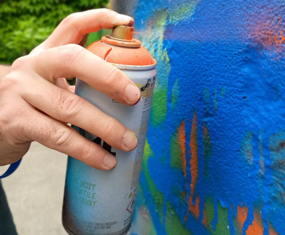 Hand spray-painting colorful graffiti on wall.