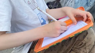 Person writing on paper with pencil outdoors.