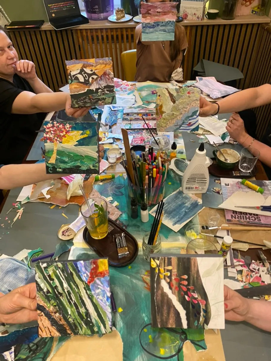 Personen halten bunte Kunstwerke am Tisch.