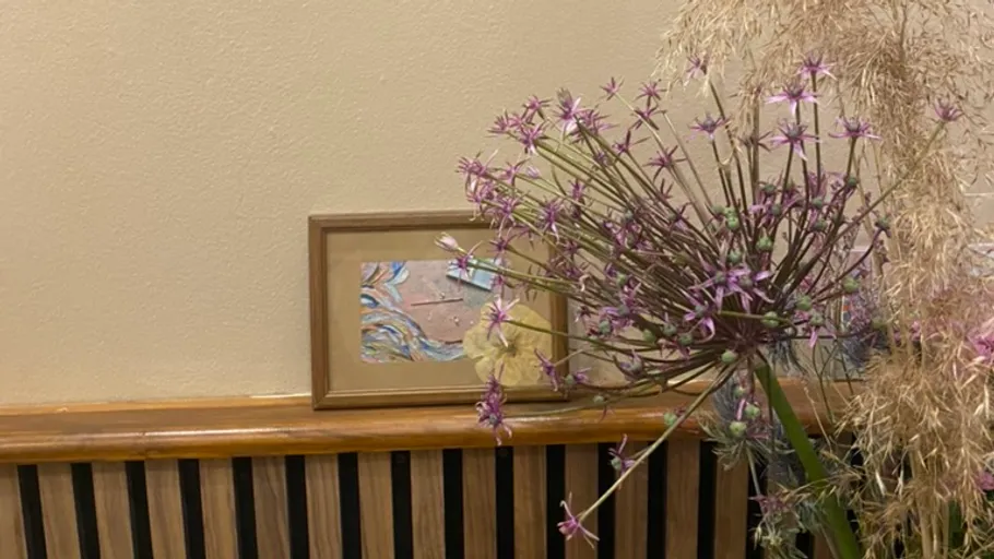 Dry flowers in vase near framed artwork.