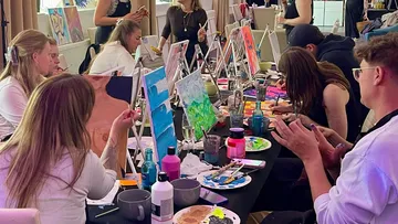 People painting canvases in a workshop setting.