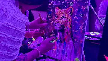 Person malt Leopard unter violettem Licht.