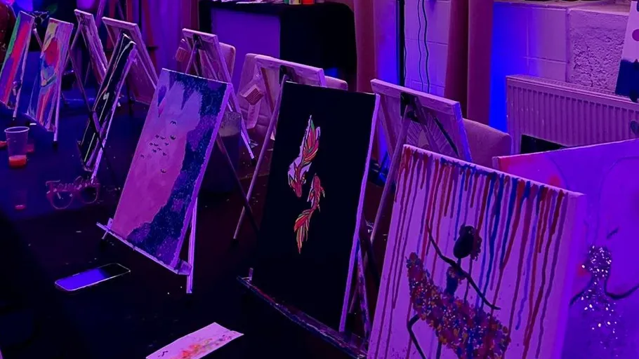 Paintings on easels under purple lighting.