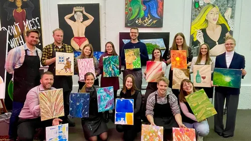 Group holding paintings in art studio.