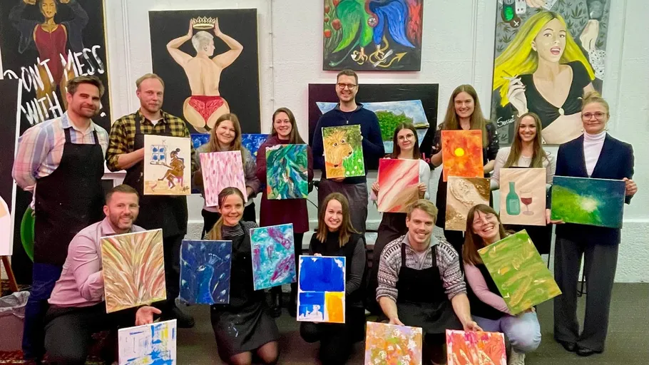 Group holding paintings in art studio.