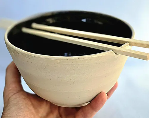 Hand holds bowl with chopsticks, simple design.