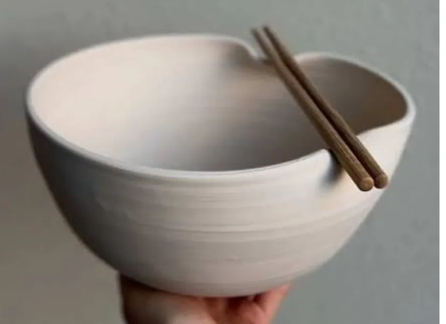 Ceramic bowl with chopsticks held in hand.