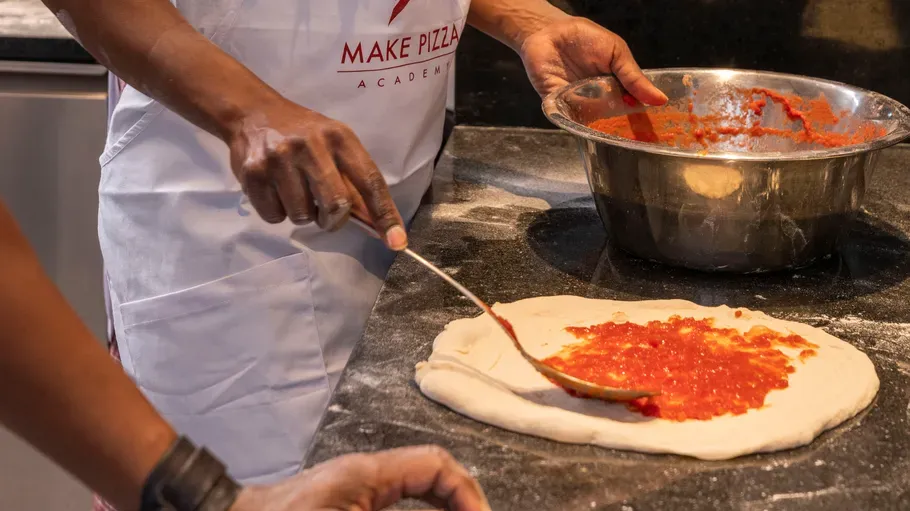 Person spreading tomato sauce on pizza dough.
