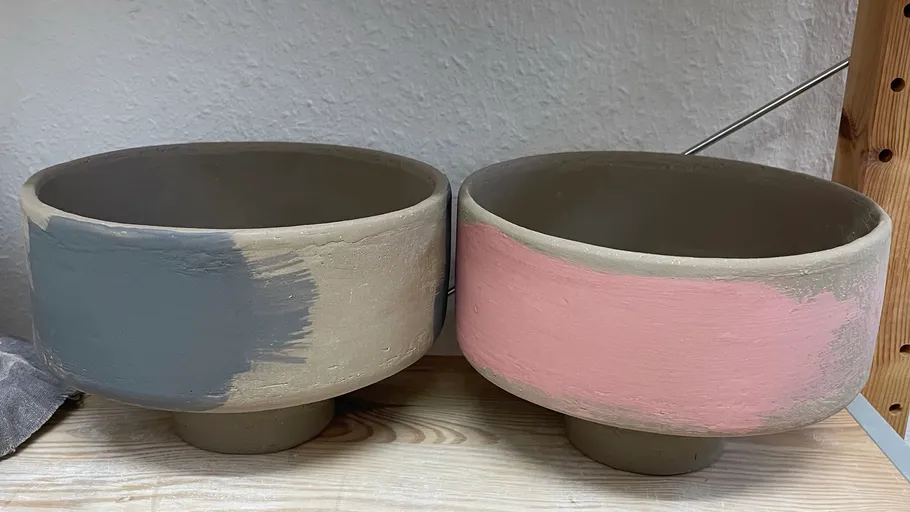 Two painted ceramic bowls on wooden shelf.