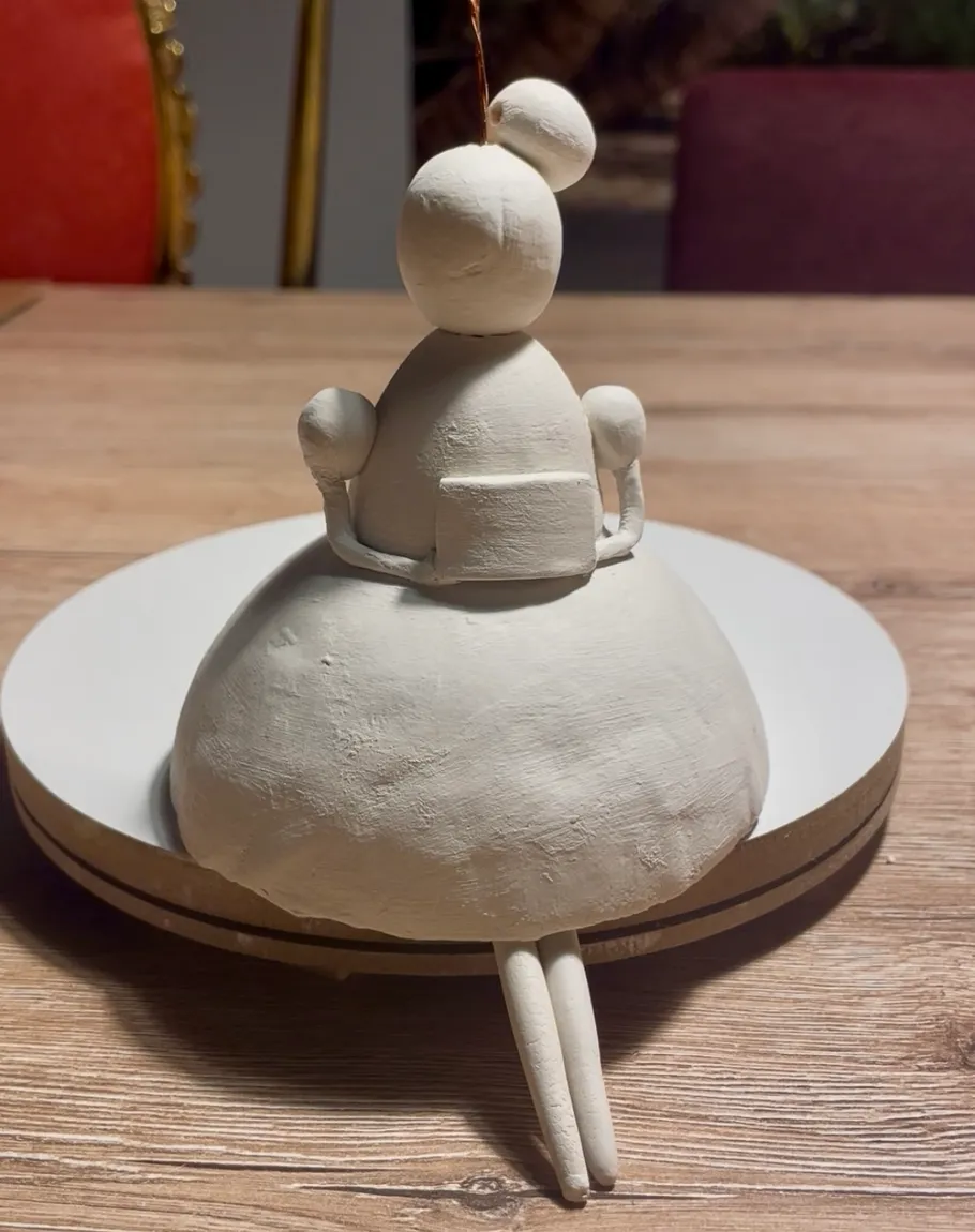 Clay figure seated on a wooden table.
