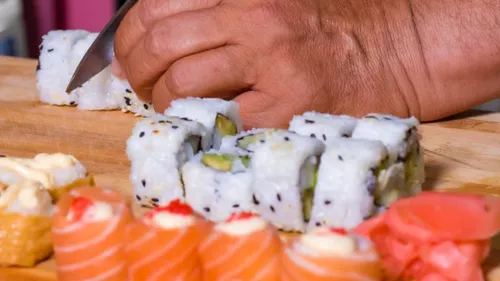 Hand schneidet Sushi auf Holzbrett.