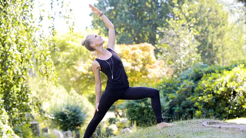 Frau praktiziert Yoga draußen im sonnigen Park.