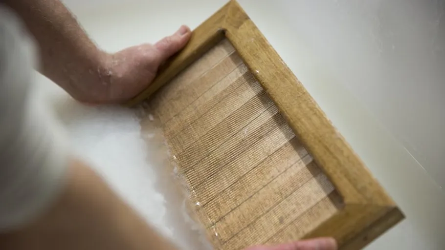 Hands holding wooden frame in water.