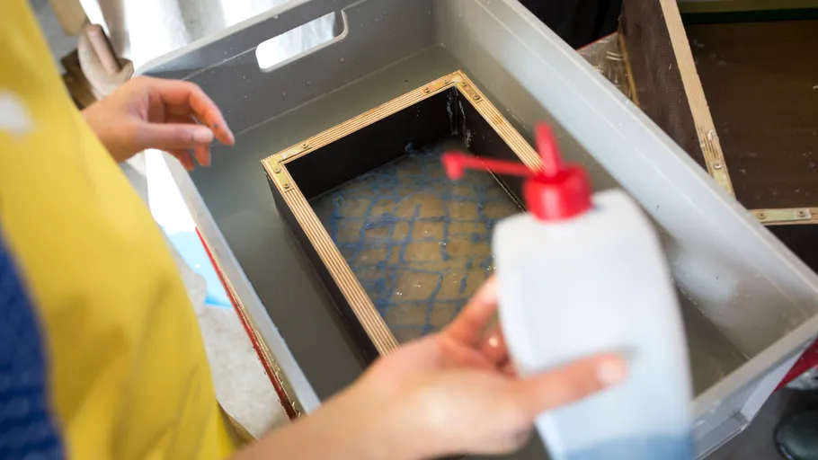 Person preparing paper pulp in water basin.