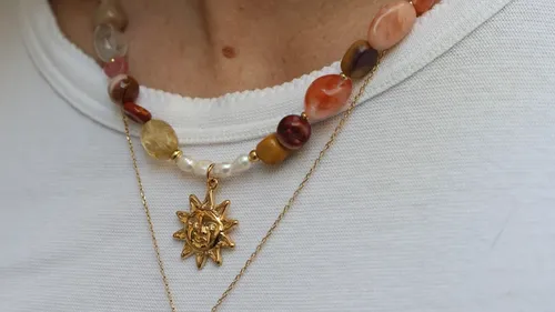 Necklace with gemstones and sun pendant on shirt.