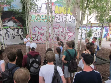 Gruppe von Jugendlichen hört einem Sprecher vor Graffiti-Wänden zu.
