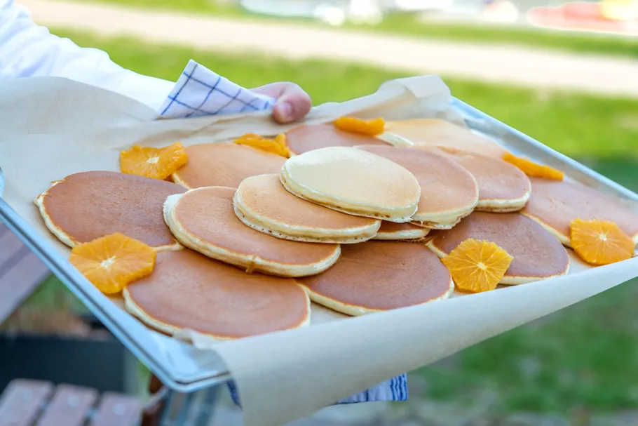 Pancakes with orange slices on a tray outdoors.