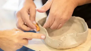 Hands shaping a clay bowl on table.