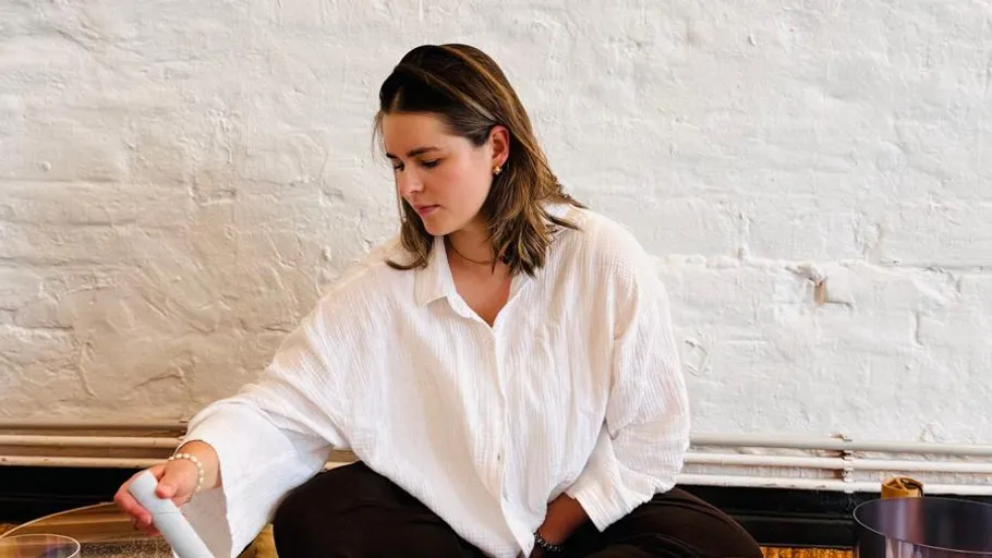 Woman sitting, pouring liquid, white brick wall.