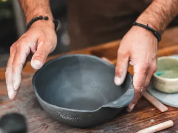 Hands form a gray ceramic bowl on a table.