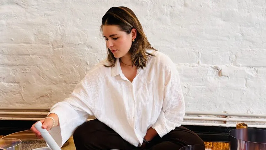 Woman sitting, playing musical instrument, white brick wall.