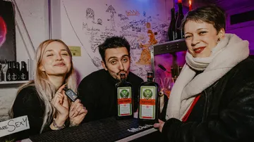 Drei Personen posieren mit Jägermeister-Flaschen in Bar.
