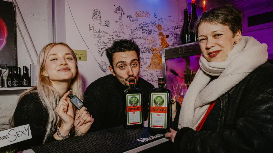 Drei Personen posieren mit Jägermeister-Flaschen in Bar.